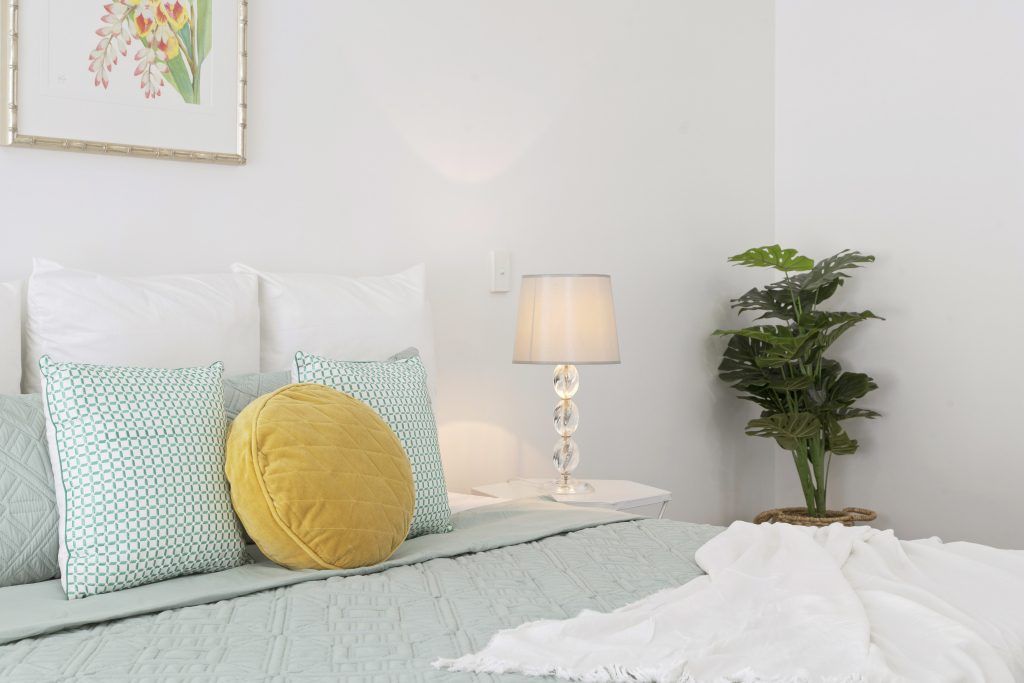 A bedroom with a bed , pillows , a lamp and a plant.