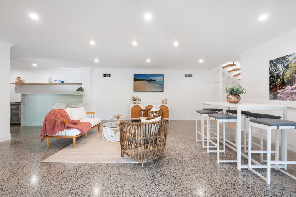 Bright living-dining room with woven chairs, white walls, recessed lights, and a small kitchen bar with stools