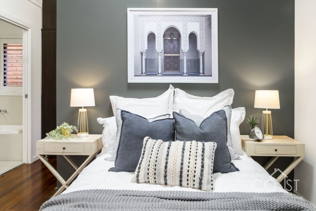 A bedroom with a bed , nightstands , lamps and a picture on the wall above the bed.