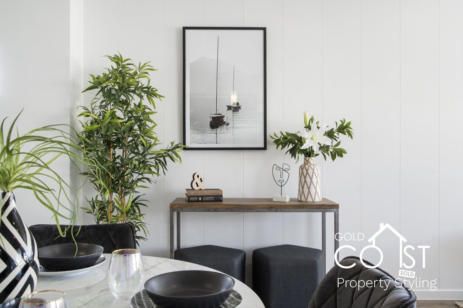 A dining room with a table , chairs , plants and a picture on the wall.