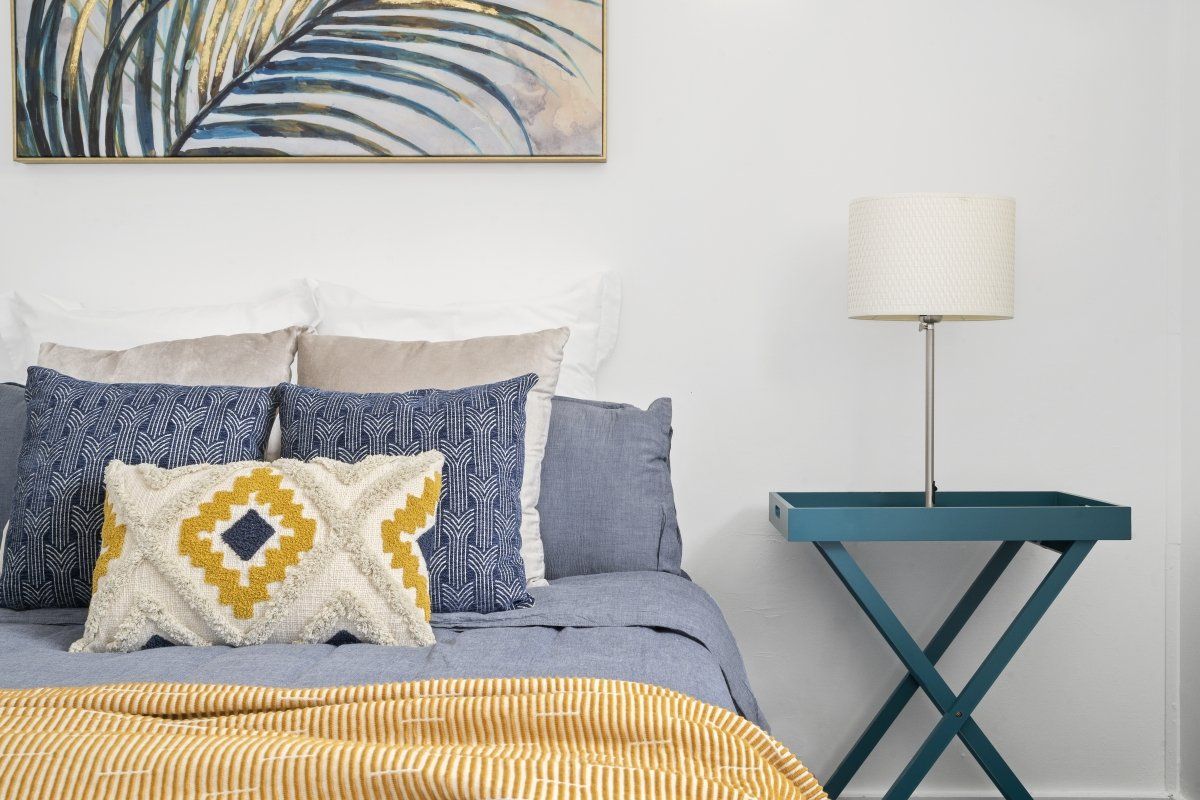 A bedroom with a bed , nightstand , lamp and painting on the wall.