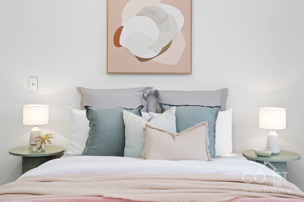 A bedroom with a bed , lamps , pillows and a painting on the wall.