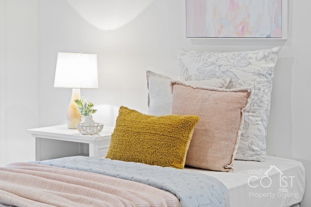 A bedroom with a bed , nightstand , lamp and pillows.