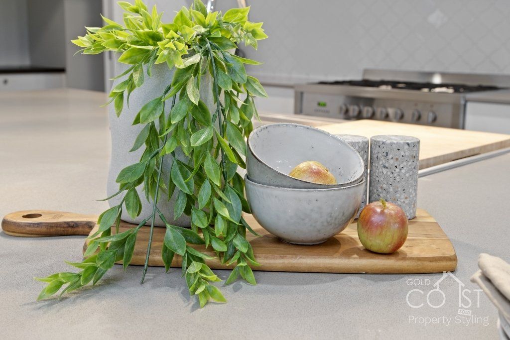 A wooden cutting board with bowls , apples and a plant on it.