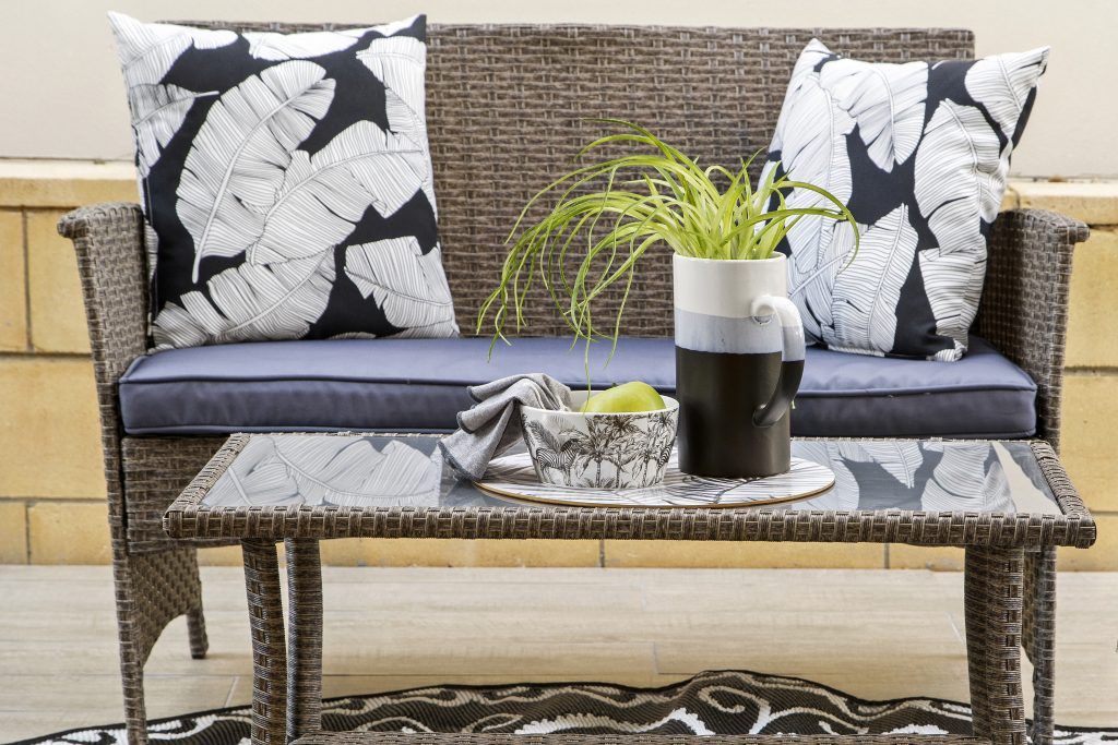 A wicker couch with black and white pillows and a coffee table