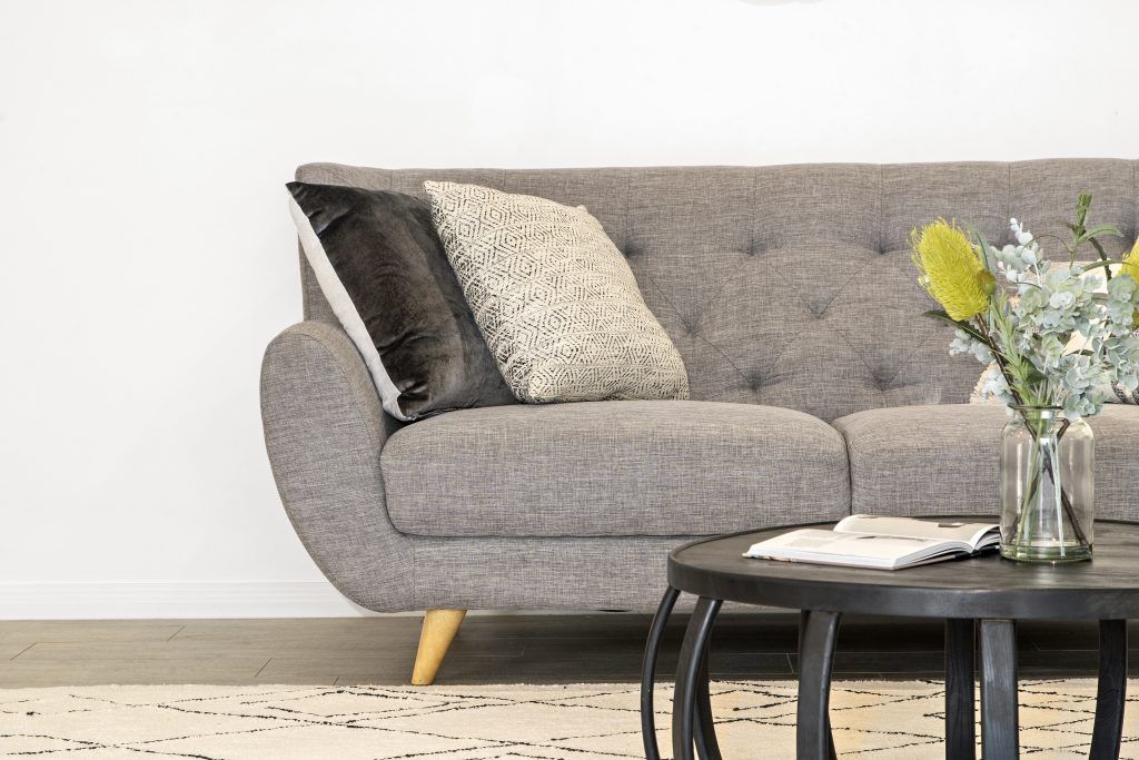 A living room with a couch , coffee table , and vase of flowers.
