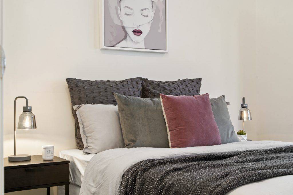 A bedroom with a bed , nightstand , lamp and painting on the wall.