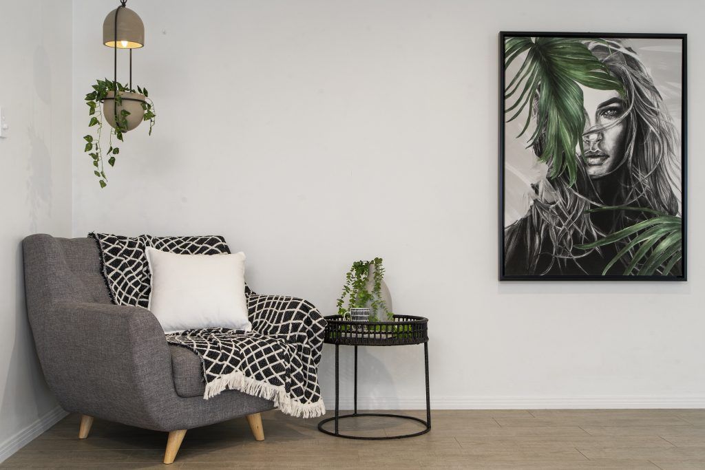 A living room with a chair , table and a painting on the wall.