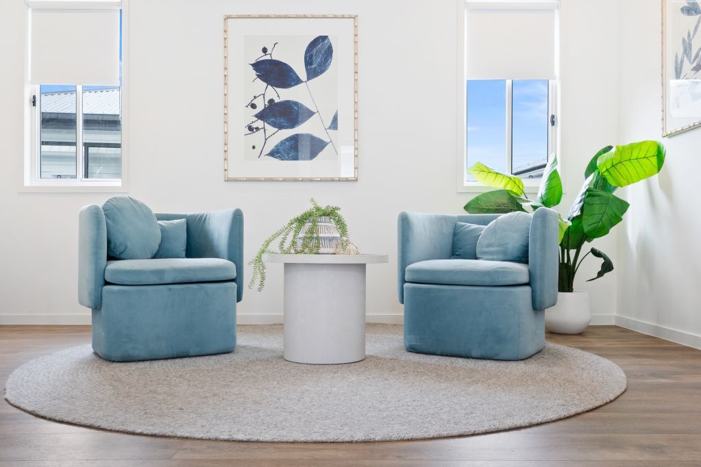 Bright living room with two blue armchairs, round rug, plant, and framed wall art