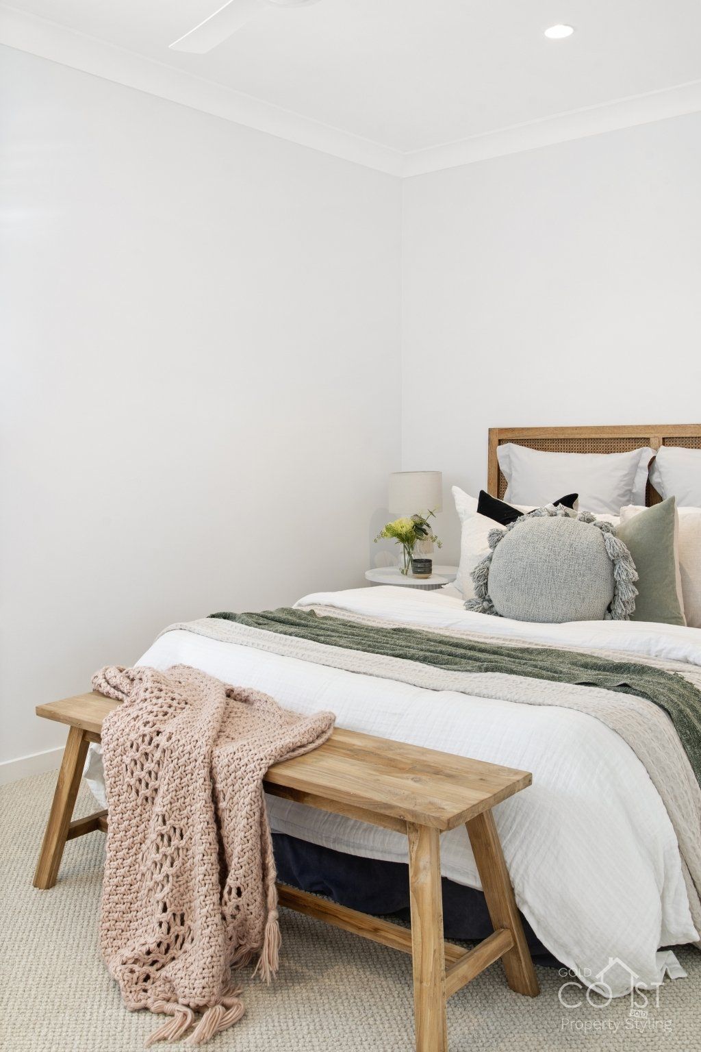 A bedroom with a bed , bench , blankets and pillows.