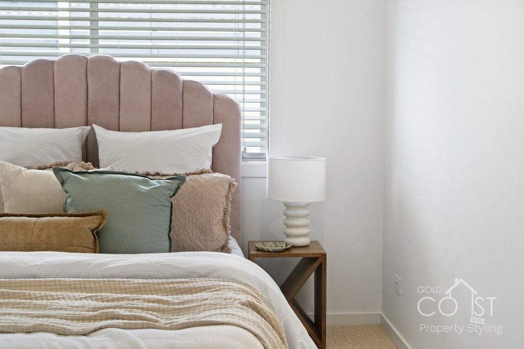 A bedroom with a bed , nightstand , lamp and window blinds.