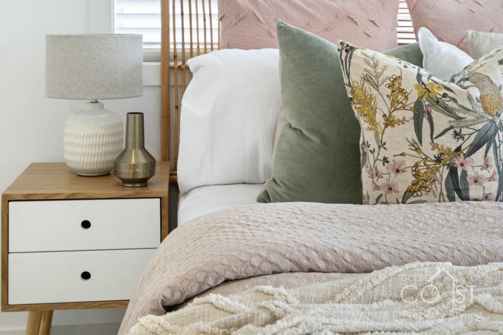 A bedroom with a bed , nightstand , lamp and pillows.