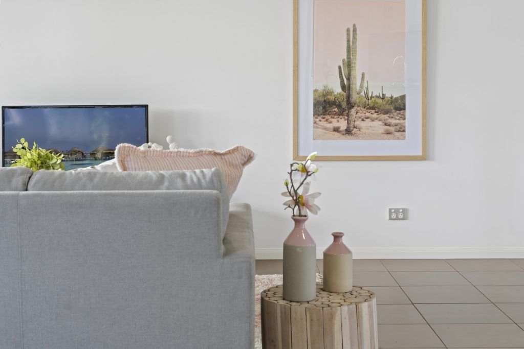 A living room with a couch , table , vases and a picture on the wall.