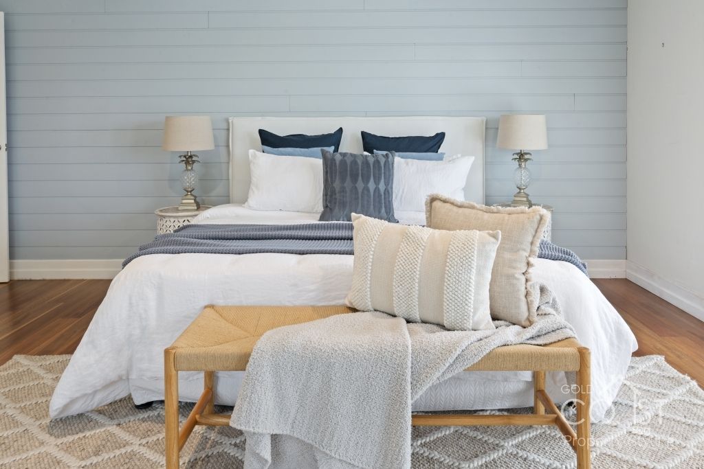 A bedroom with a bed , bench , lamps and a rug.