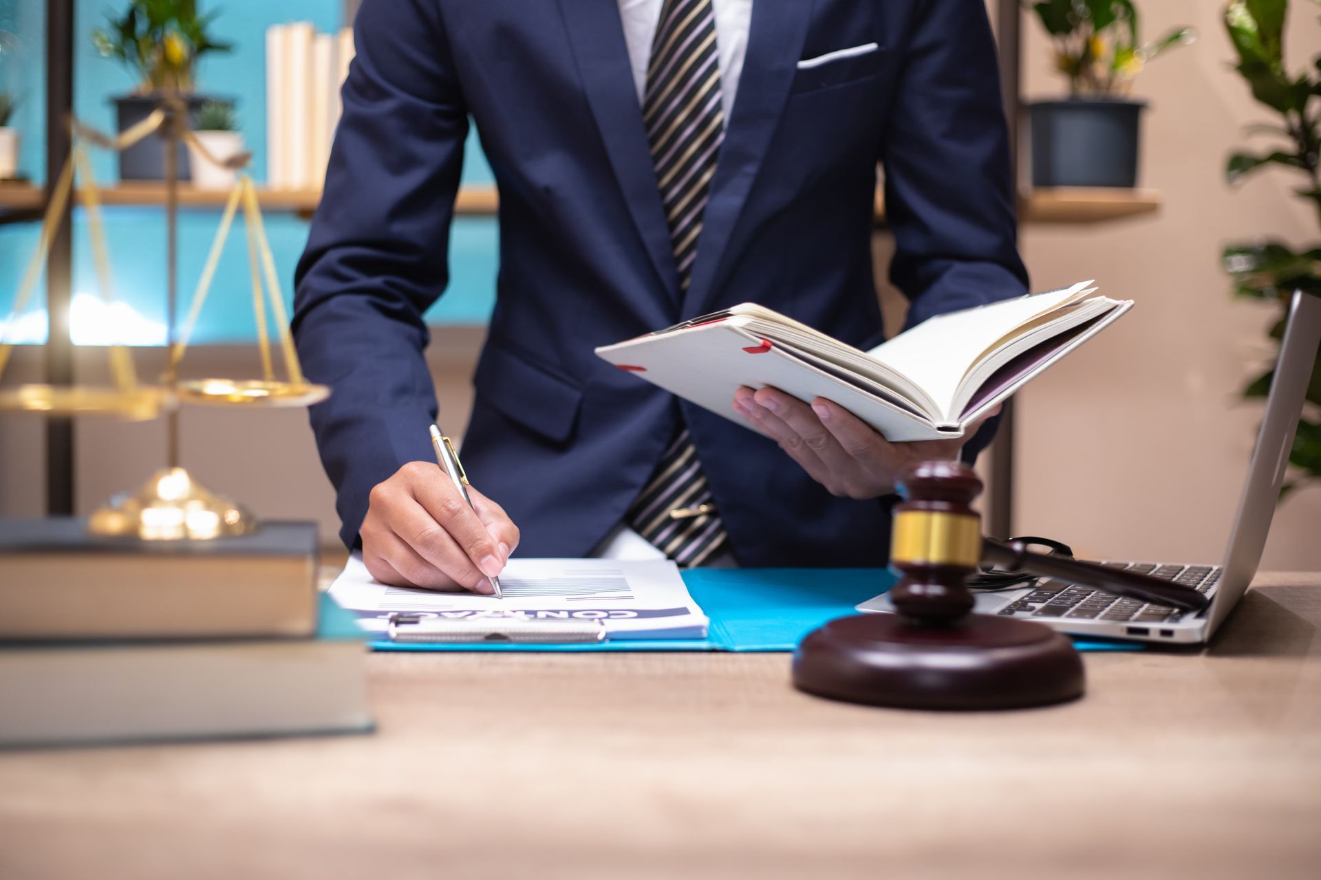 Lawyer in suit taking notes at desk with law books, scales of justice, and gavel.