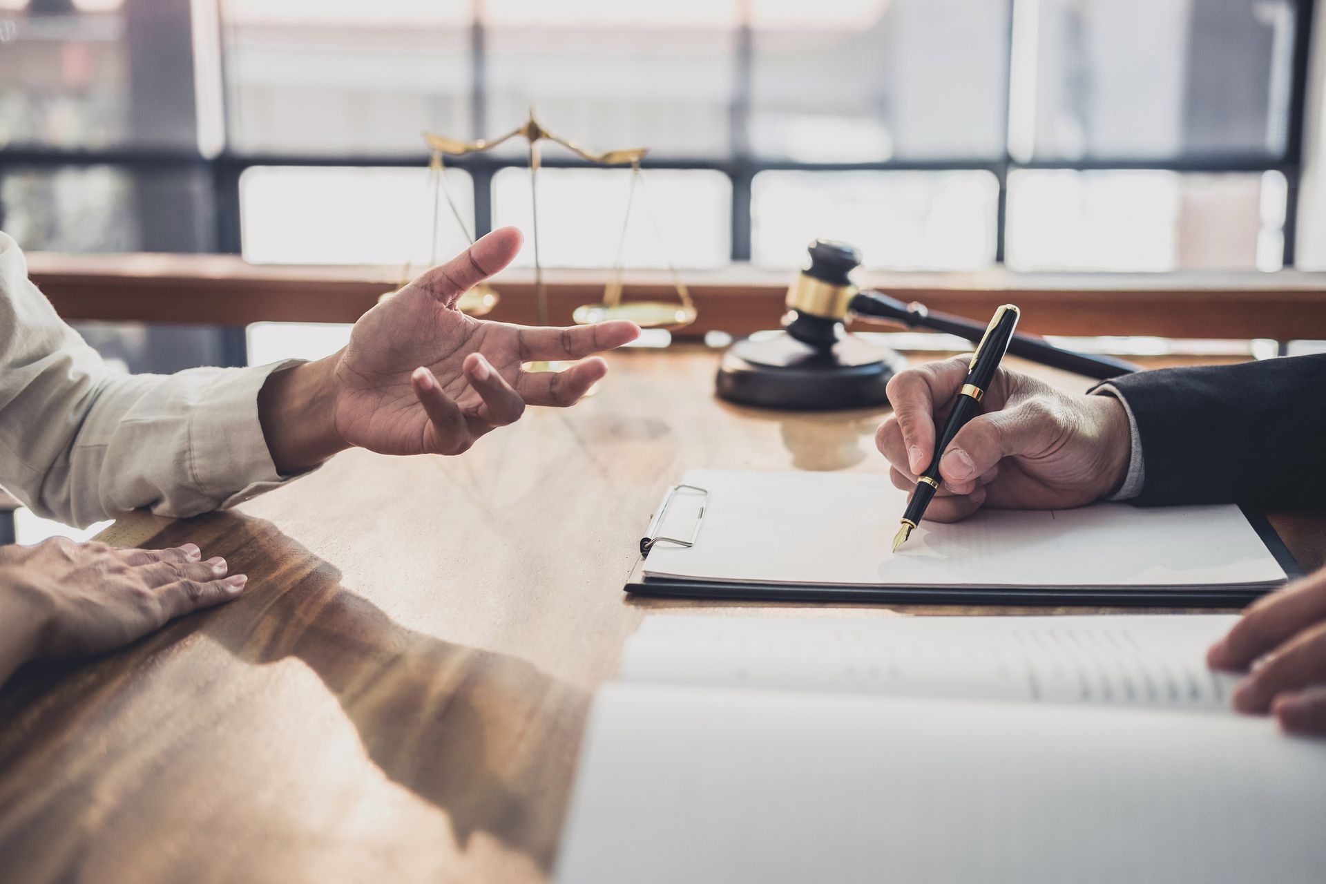 Two people at a desk; one gestures while the other signs a document, scales and gavel in the background.