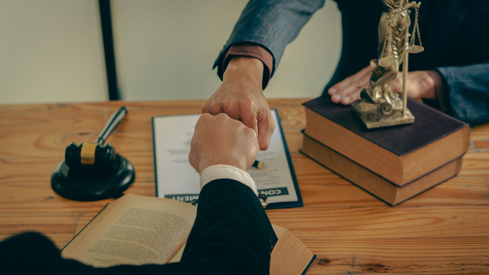 Two people in suits fist bump over a contract and law books.