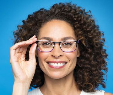 A woman with curly hair is wearing glasses and smiling.