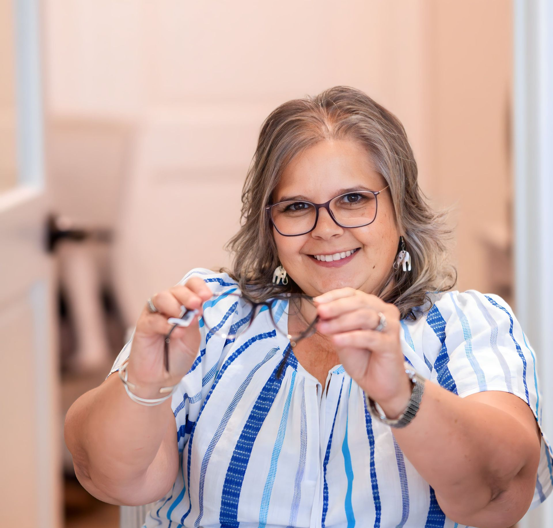 A woman with curly hair is wearing glasses and smiling.