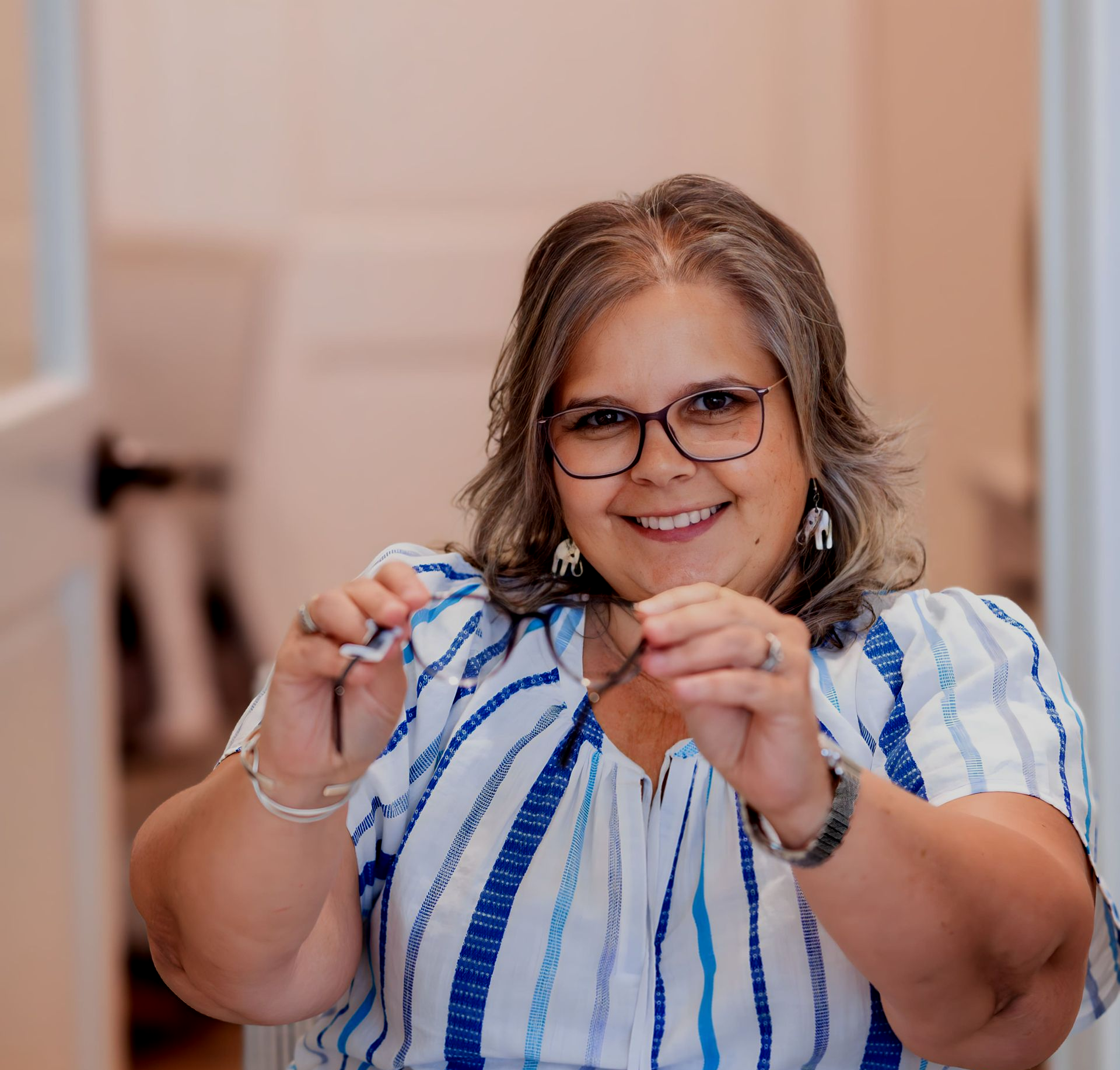 A woman with curly hair is wearing glasses and smiling.