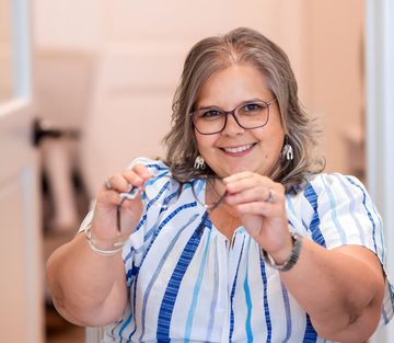 A woman with curly hair is wearing glasses and smiling.