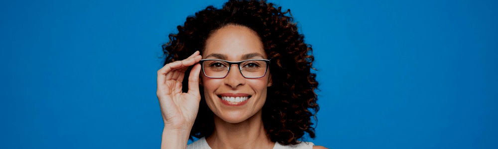 A woman with curly hair is wearing glasses and smiling.