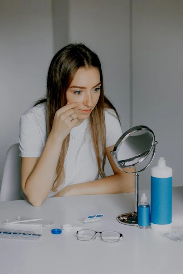 A woman is sitting at a table looking at herself in a mirror.