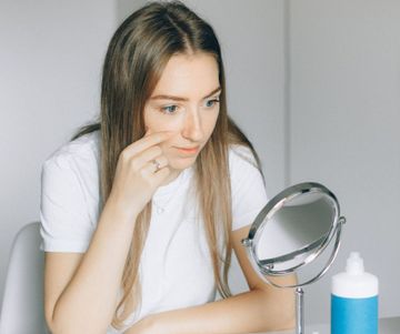 A woman is looking at her face in a mirror.