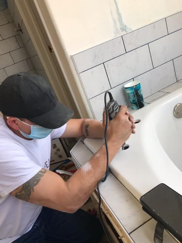 A man wearing a mask is working on a bathtub