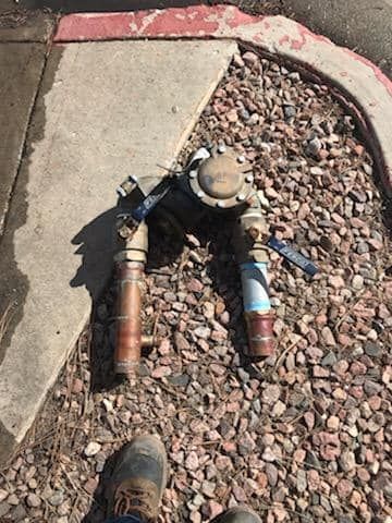 A person is standing next to a water meter on the sidewalk.