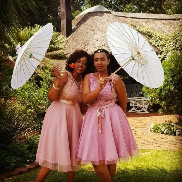 Two women in pink dresses holding white umbrellas