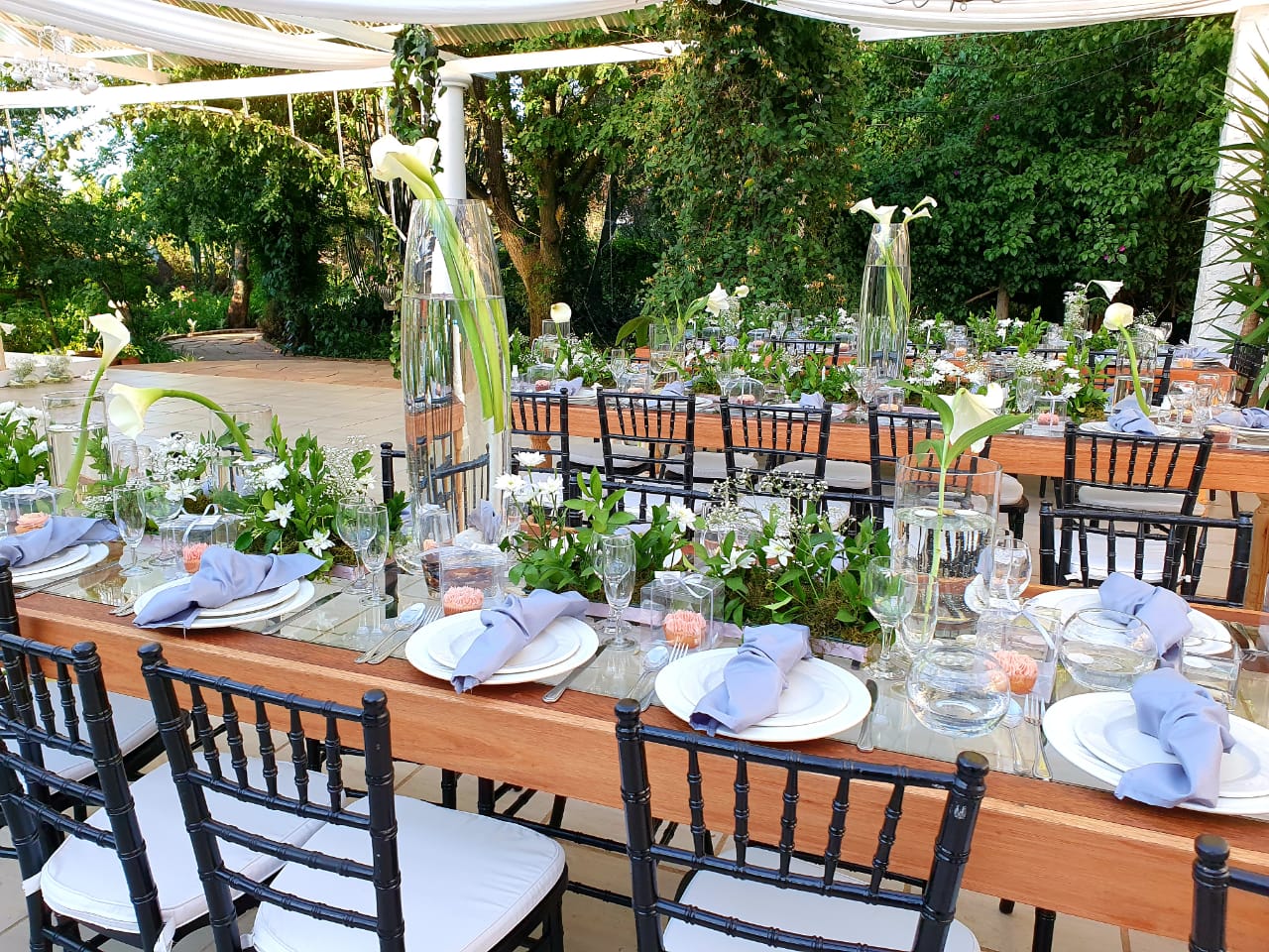A long table with plates , glasses , and vases on it is set for a wedding reception.