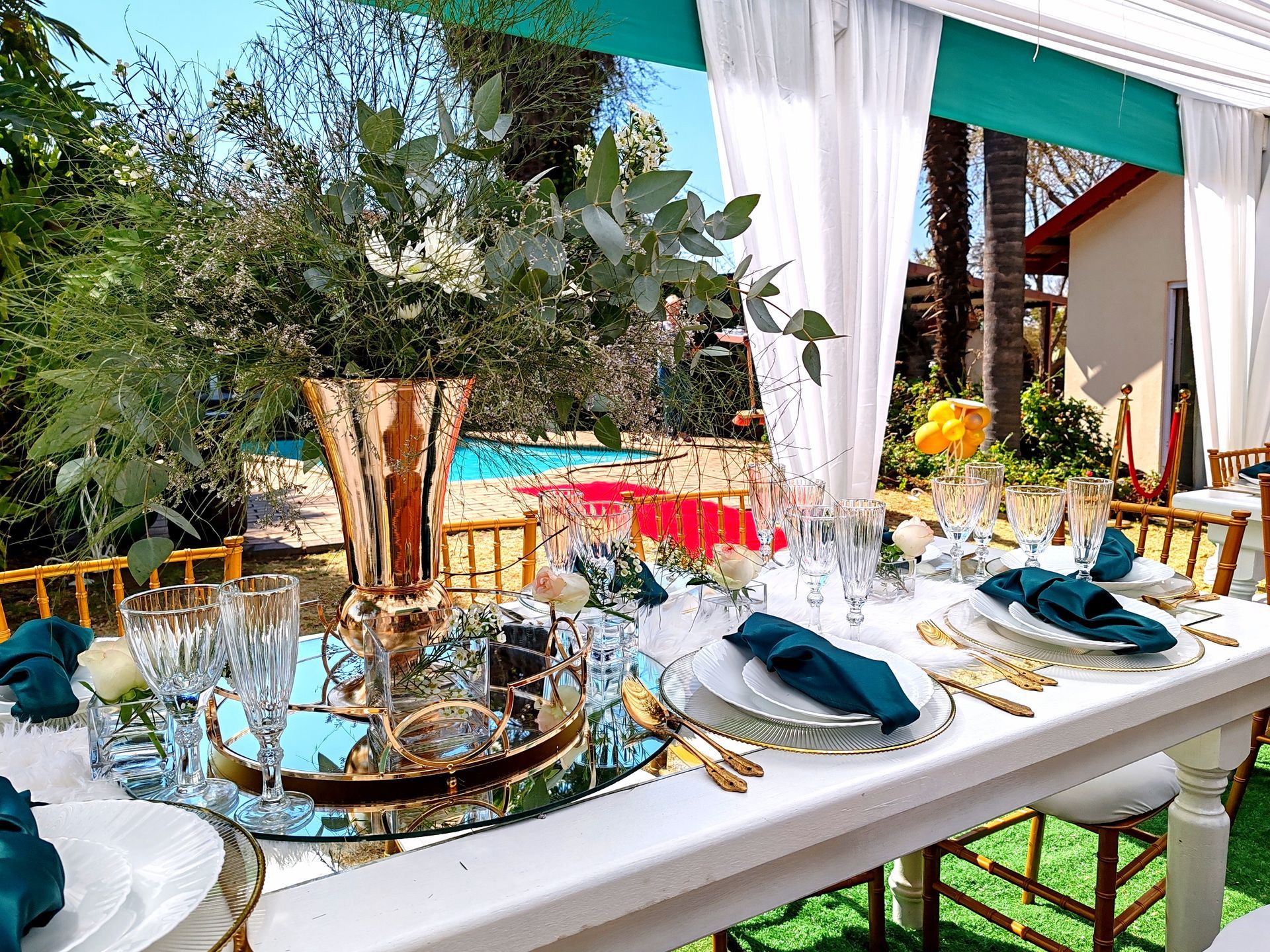A long table with plates , utensils , and a vase on top of it.