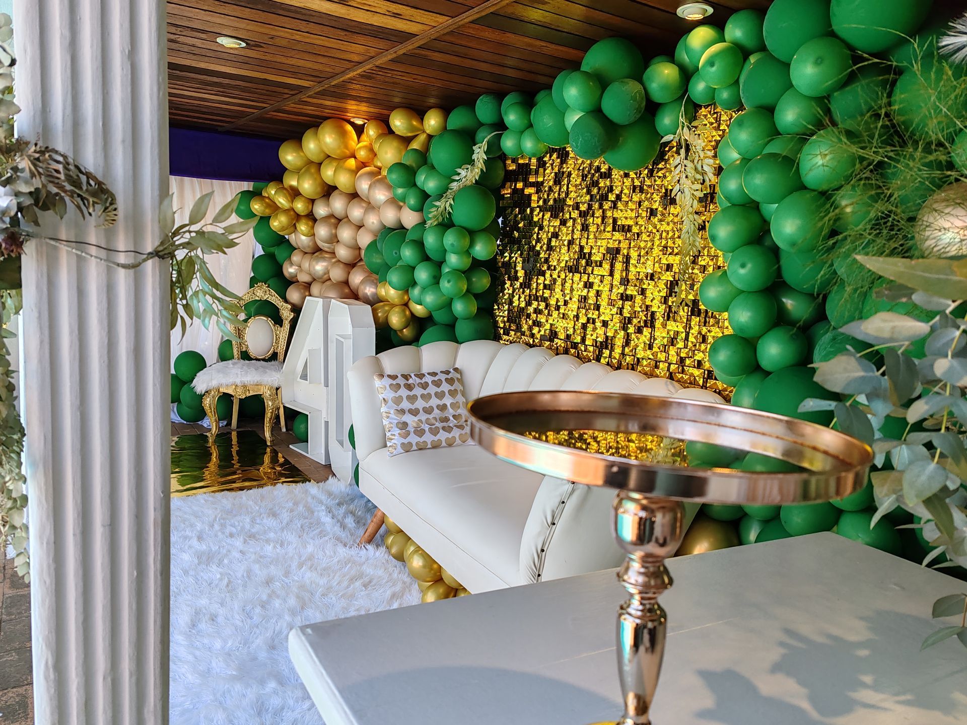 A room filled with green and gold balloons and a couch.