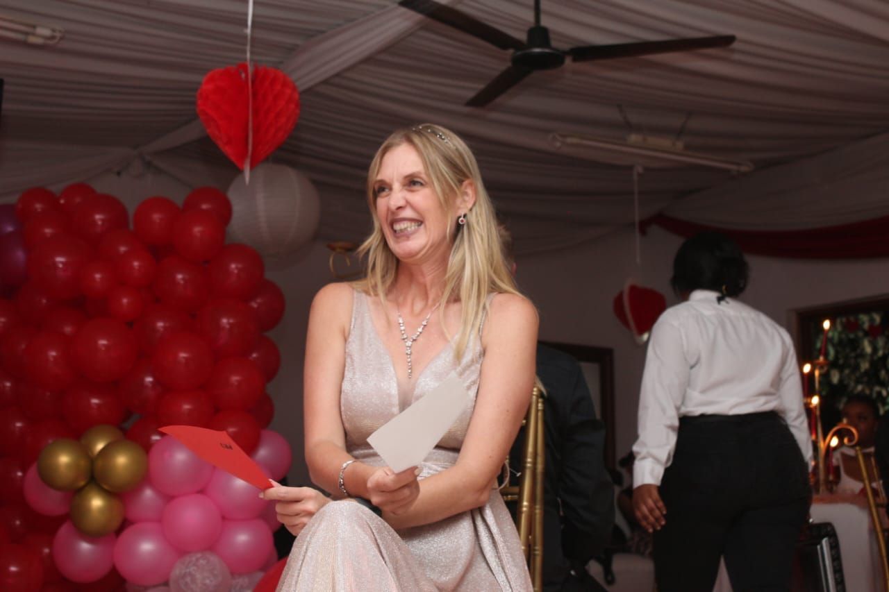 A woman is sitting in front of a wall of balloons holding a piece of paper.