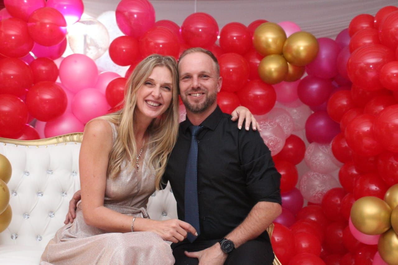 A man and a woman are posing for a picture in front of a wall of balloons.