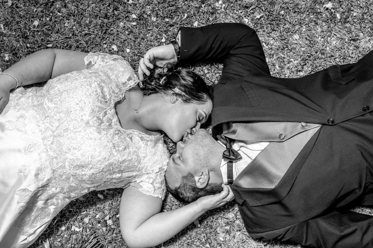A bride and groom are laying on the ground and kissing.