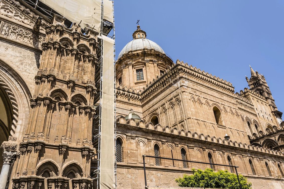 L'esterno in pietra color ocra e la cupola centrale del Duomo di Palermo, riccamente decorate, sotto un cielo azzurro e limpido.