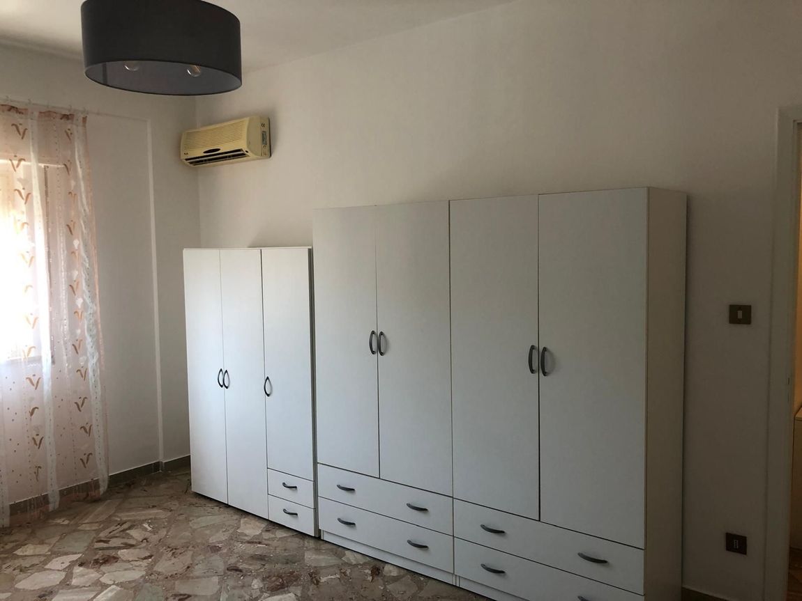 Un armadio bianco con cassetti, appoggiato a una parete bianca in una stanza con pavimento a motivi geometrici 