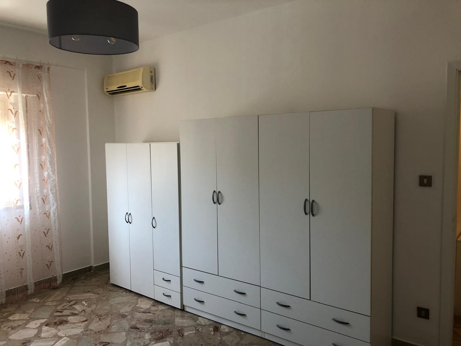 Un armadio bianco con cassetti, appoggiato a una parete bianca in una stanza con pavimento a motivi geometrici 