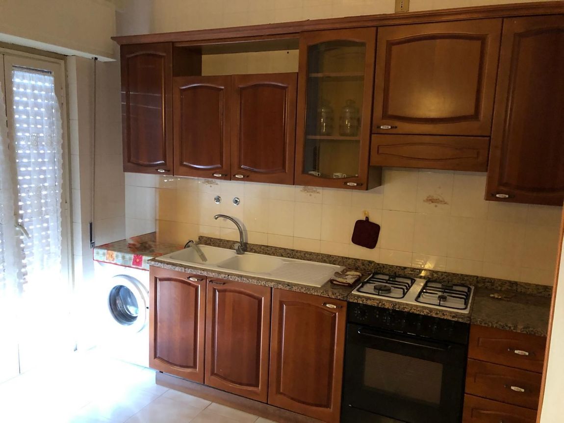 Una cucina con mobili in legno, lavello, piano cottura a gas con forno e lavatrice accanto a una porta luminosa.