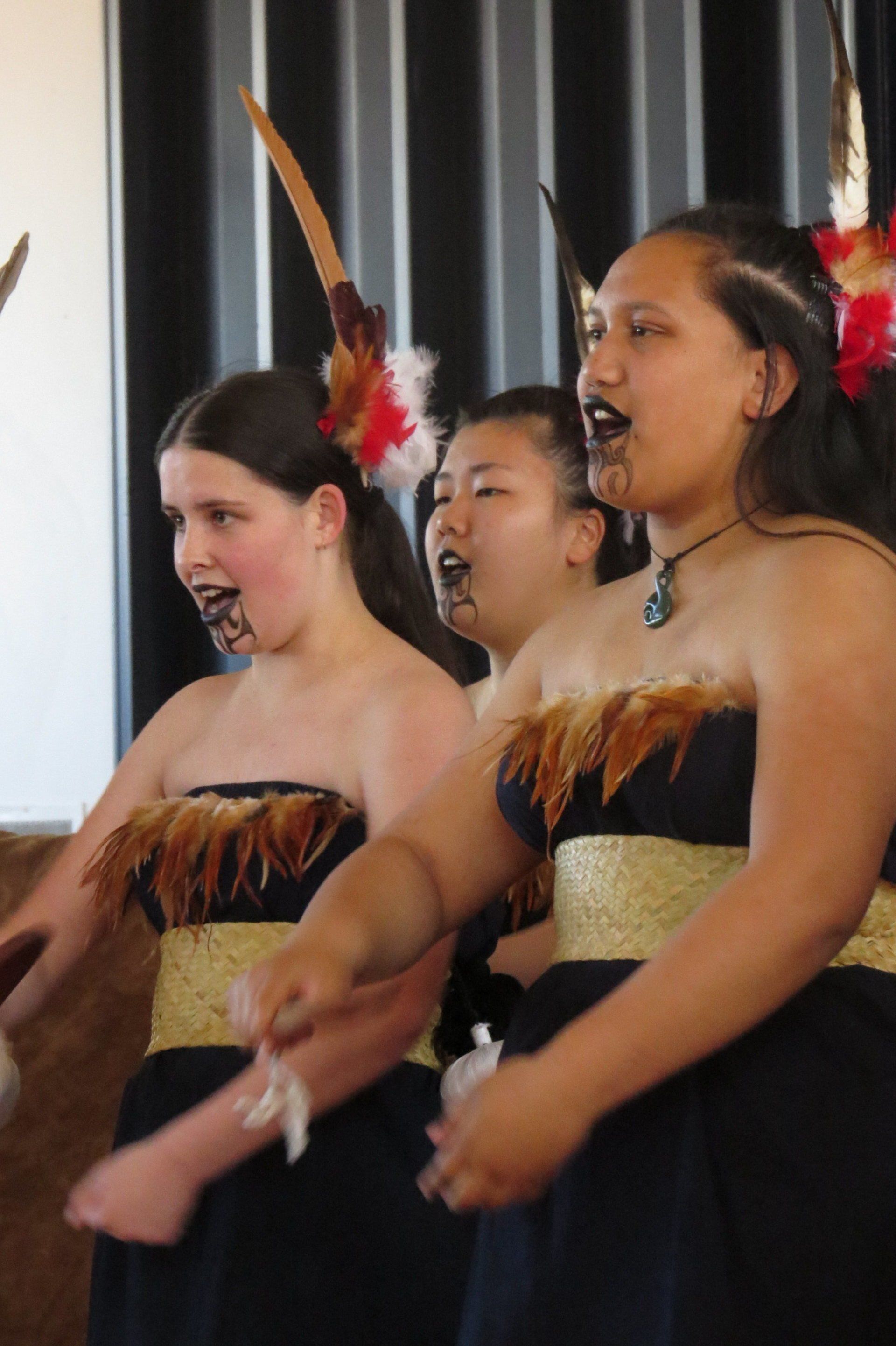 A group of young women singing in a choir with feathers in their hair