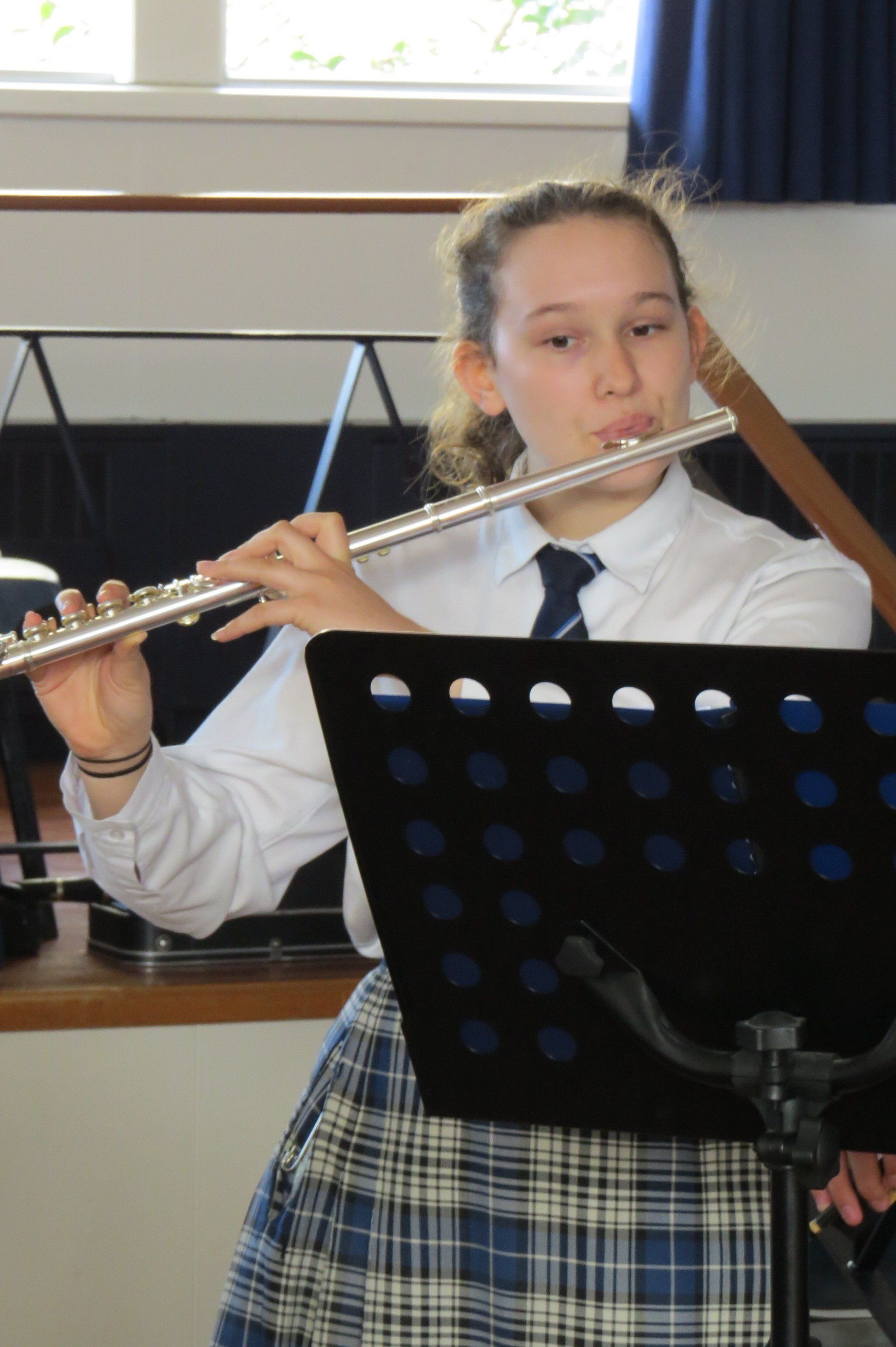 A girl in a plaid skirt is playing a flute