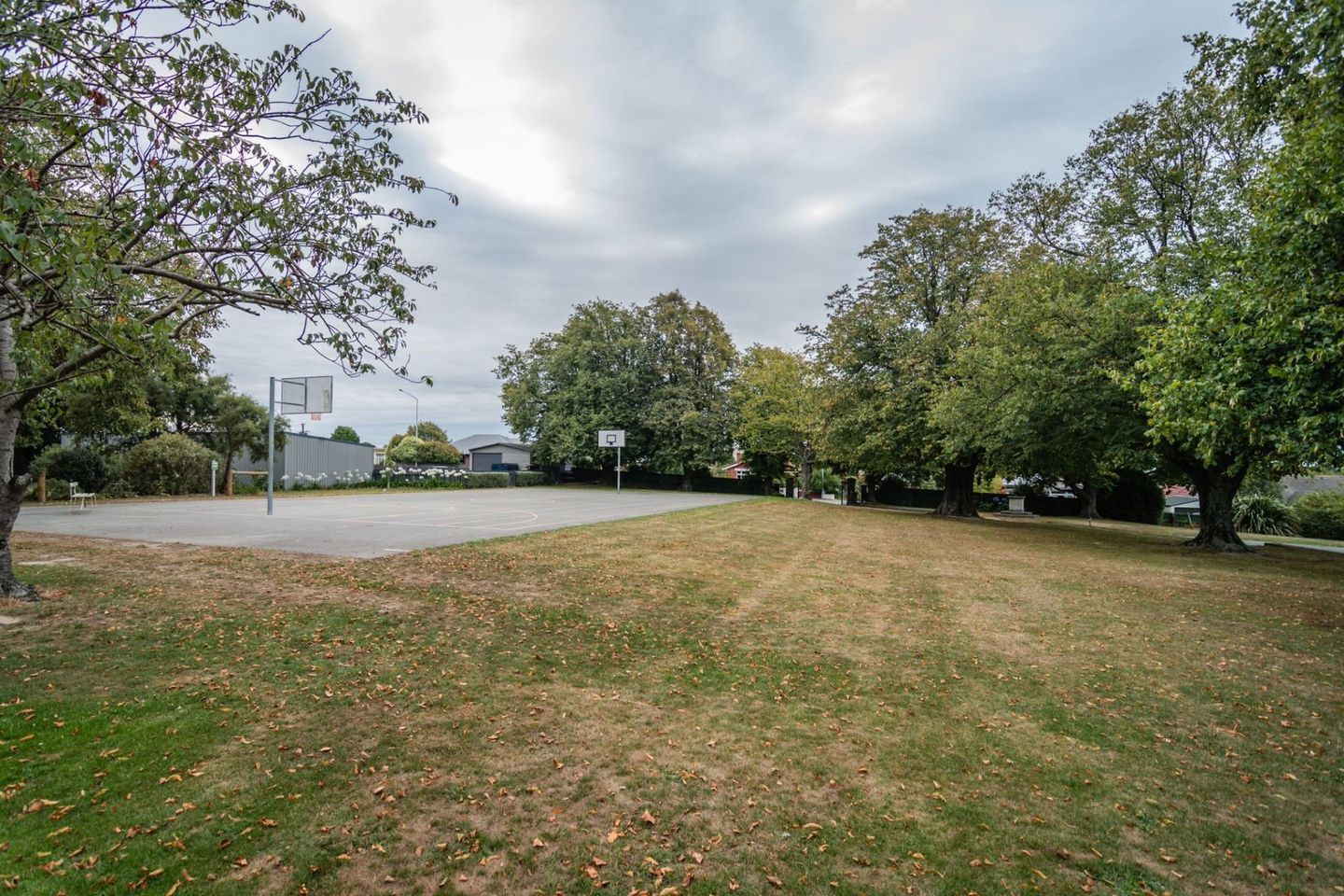Timaru Girls Hig School | There is a basketball court in the middle of a park surrounded by trees.