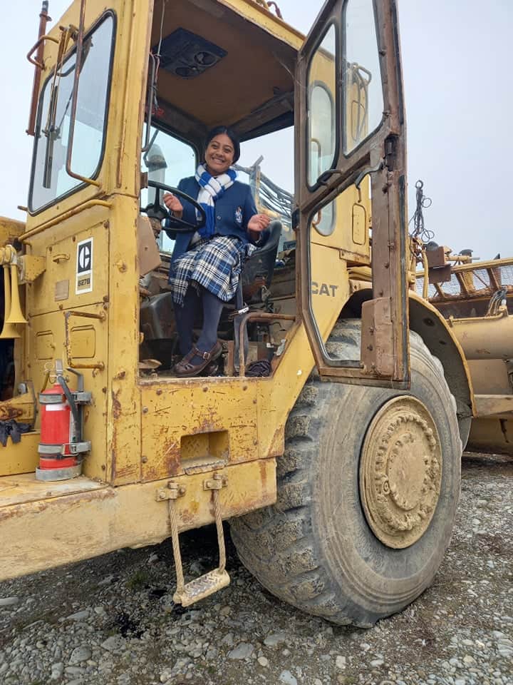 A woman is sitting in the driver 's seat of a yellow caterpillar bulldozer.