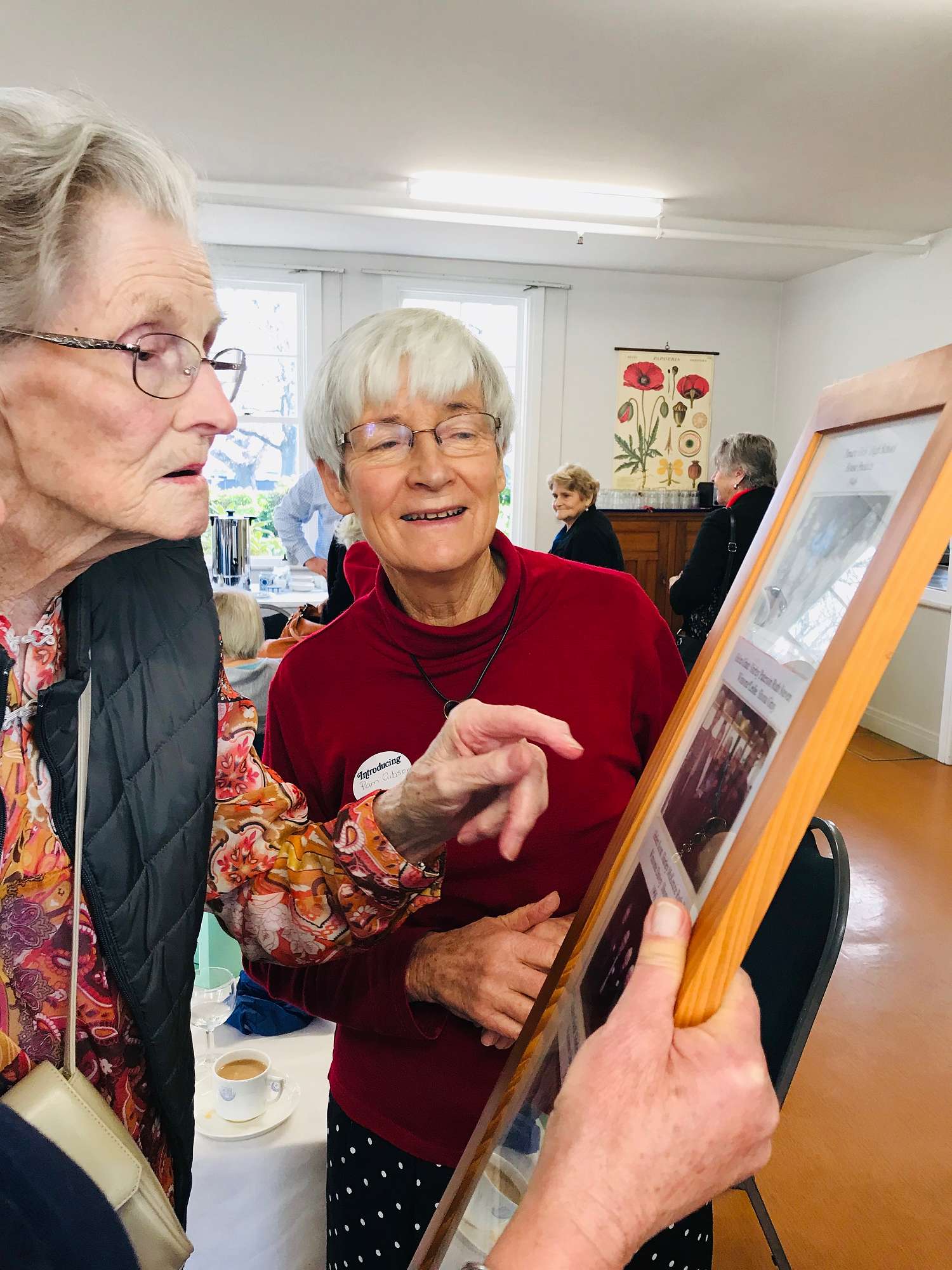 Two older women are looking at a framed picture in a room.