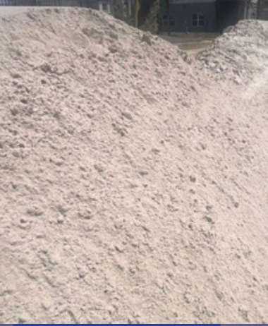 A large, light-colored mound of coarse sand or gravel sits against an outdoor background.