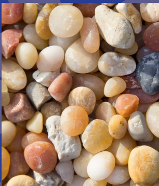 A close-up view of smooth, multicolored river rocks and pebbles in shades of tan, peach, gray, and white.
