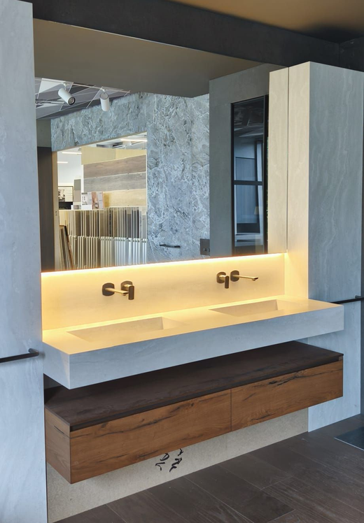 Bagno moderno e accessibile con due WC, piastrelle grigie e portasciugamani accanto allo specchio.