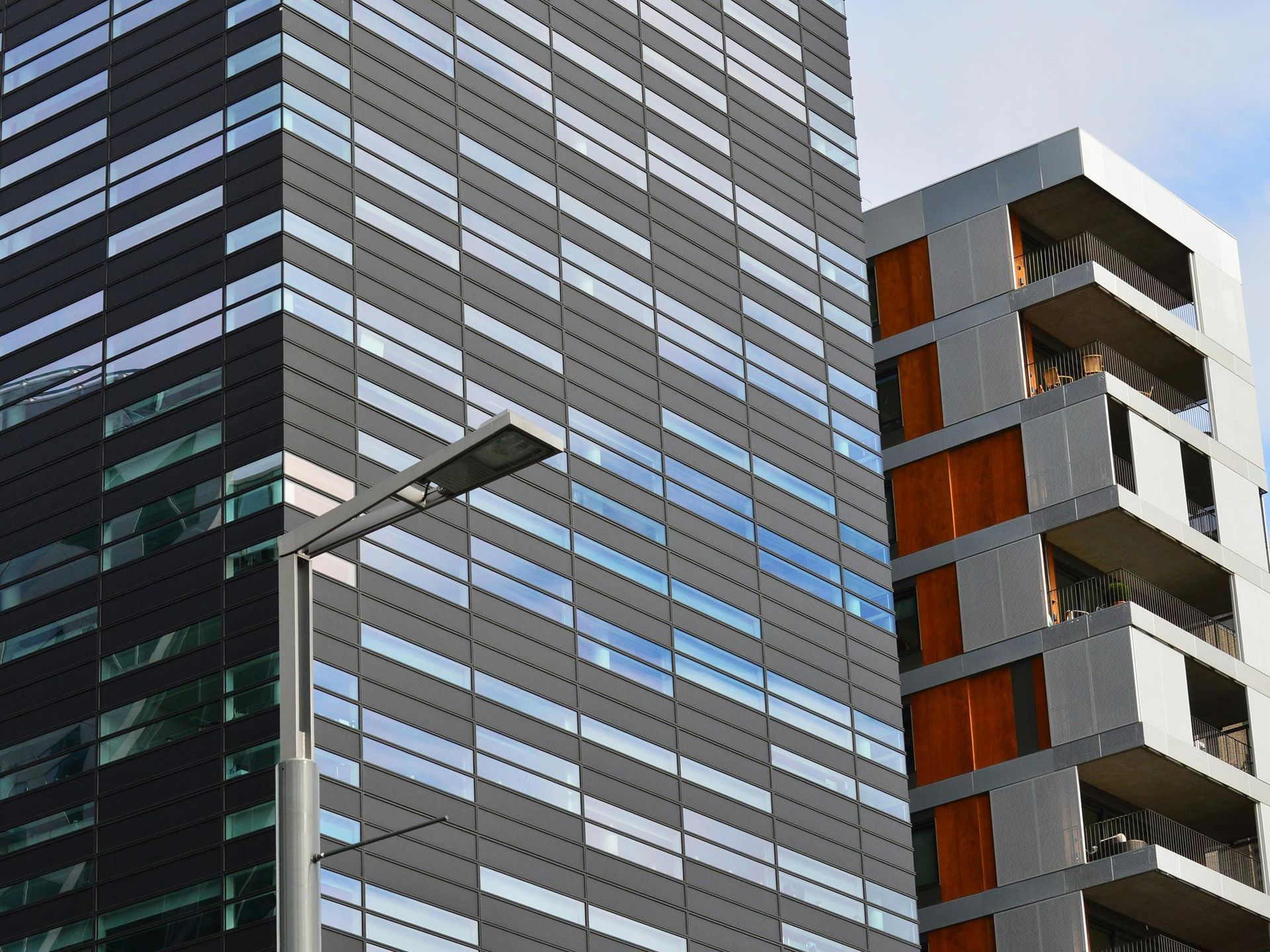 Two modern skyscrapers with glass and dark gray facades; lamppost in foreground.